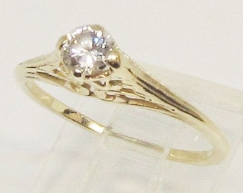 May include: A gold ring with a single round diamond set in a delicate, ornate design.