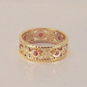 May include: A gold band ring with a delicate filigree design and small red gemstones.