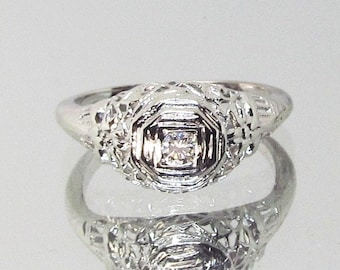 May include: A silver filigree ring with a small, clear diamond in the center.