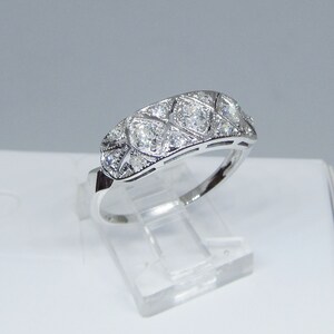 May include: A silver band ring with a row of small, clear diamonds set in a geometric pattern.