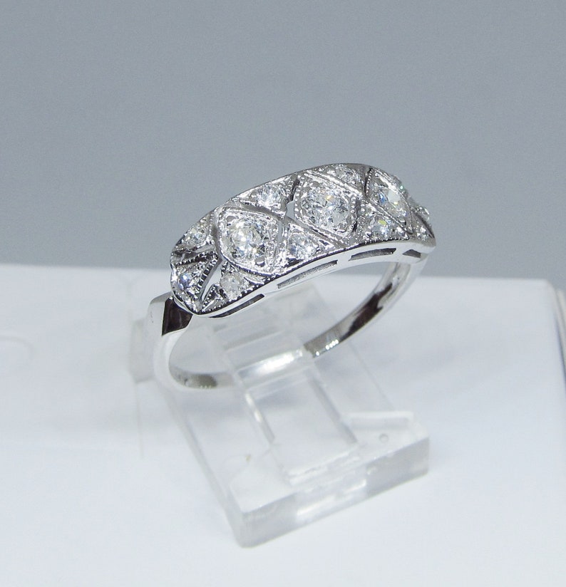May include: A silver band ring with a row of small, clear diamonds set in a geometric pattern.