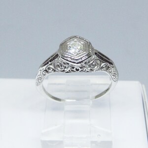 May include: A silver engagement ring with a hexagonal diamond set in a filigree design.