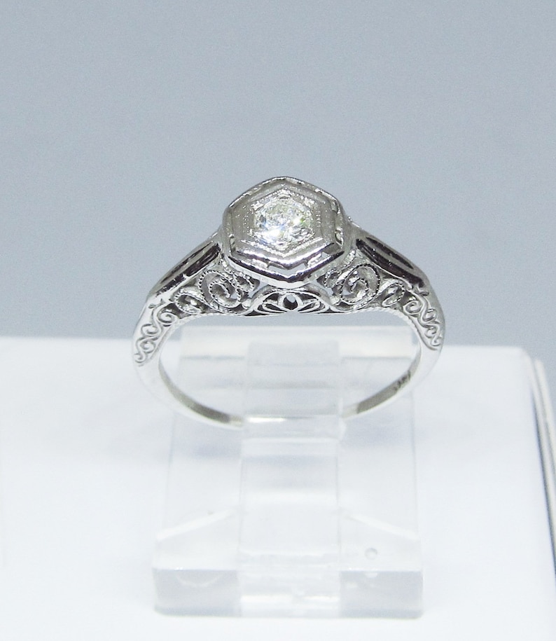 May include: A silver engagement ring with a hexagonal diamond set in a filigree design.