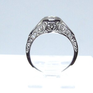 May include: A silver filigree engagement ring with a round, clear gemstone.