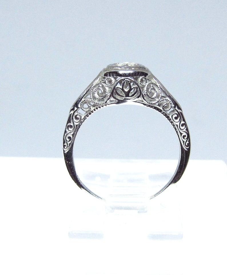 May include: A silver filigree engagement ring with a round, clear gemstone.