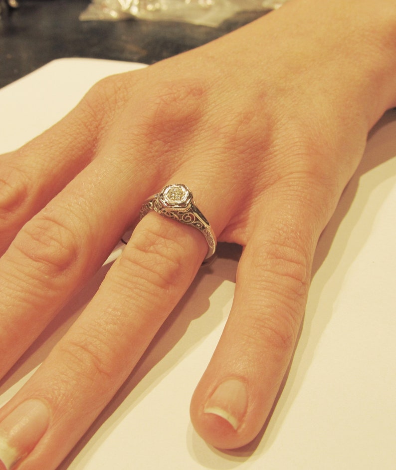 May include: A silver ring with a delicate filigree design and a single round diamond in the center.