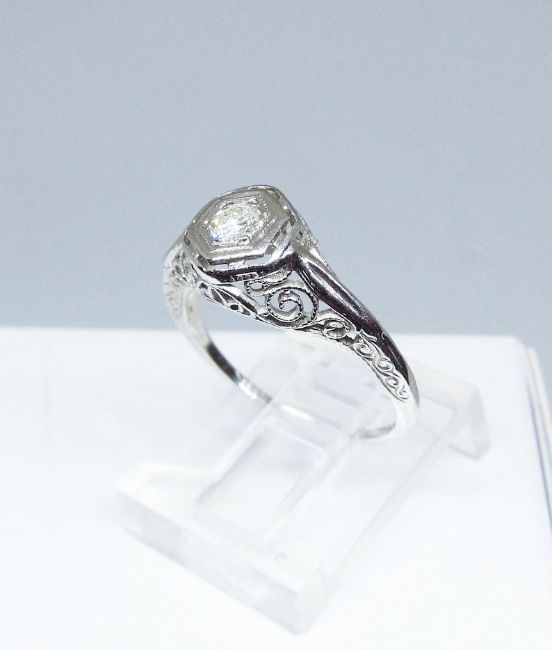 May include: A delicate silver ring with a filigree design and a small, round diamond in the center.