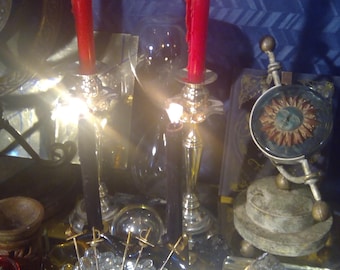 Könnte beinhalten: Zwei rote Kerzen, die in silbernen Kerzenhaltern brennen, eine klare Glasschale gefüllt mit klaren Glasperlen, eine Kristallspitze auf einem weißen Sockel und eine kleine Sonne aus Metall mit einem Gesicht auf einem Holzsockel.