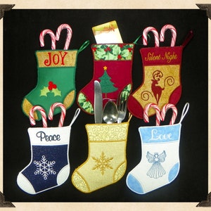 May include: A collection of six Christmas stockings in various colors, each with a unique design and message. The stockings are filled with candy canes and some contain silverware or a gift card. Messages include "Joy", "Peace", "Love", and "Silent Night".