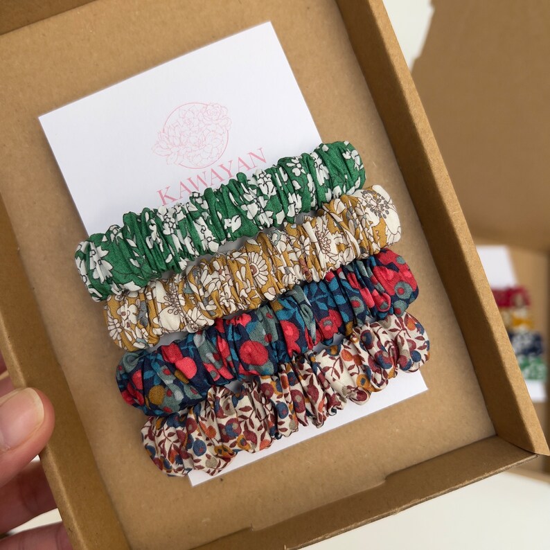 May include: A set of four floral patterned hair scrunchies in a box. The scrunchies are green, yellow, blue, and red. The box has the word "Kawayan" printed on it.