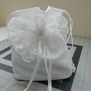 May include: White satin drawstring bag with a white lace trim and a white satin bow with a pearl embellishment.