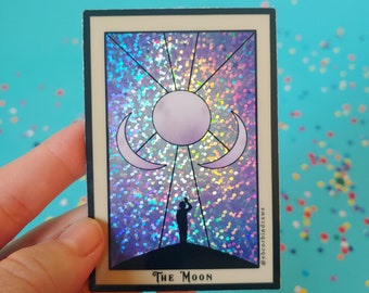 May include: A holographic sticker featuring the The Moon tarot card. The card is surrounded by a glittery, iridescent background. The card features a crescent moon, a full moon, and a figure standing on a hilltop.
