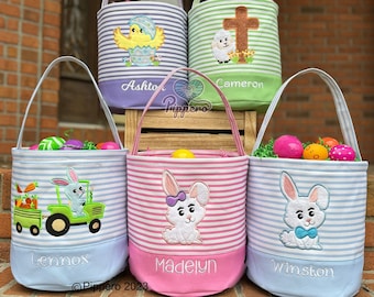 May include: Five personalized Easter baskets with different embroidered designs. The baskets are striped in blue, pink, green, and purple. The designs include a chick, a cross, a bunny pulling a tractor, and two bunnies. The baskets are labeled with the names Lennox, Madelyn, Winston, Ashton, and Cameron.