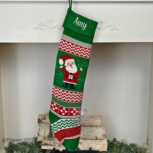 May include: Green knitted Christmas stocking with a red and white chevron pattern, a Santa Claus graphic, and the name "Amy" embroidered on the cuff.