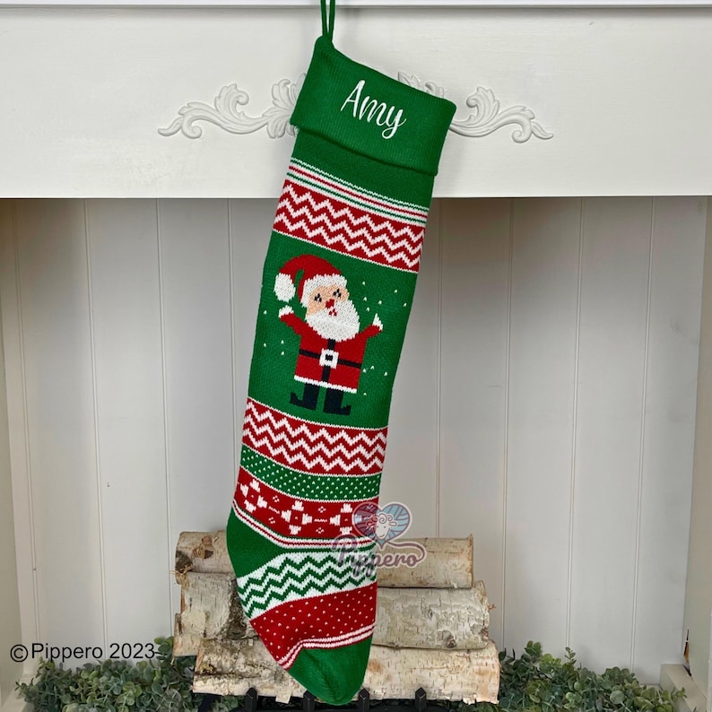May include: Green knitted Christmas stocking with a red and white chevron pattern, a Santa Claus graphic, and the name "Amy" embroidered on the cuff.