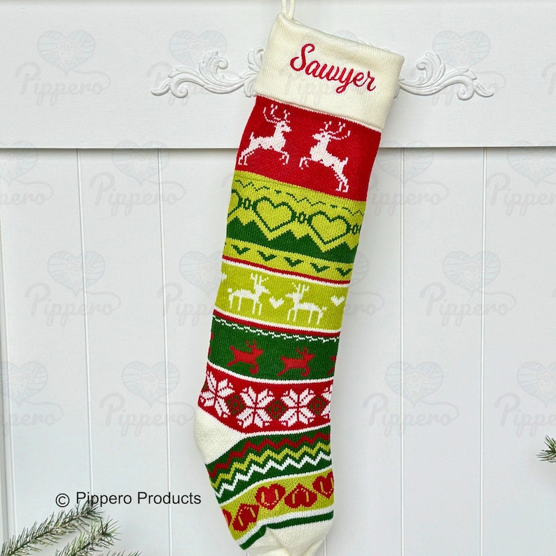 May include: A white knitted Christmas stocking with a red, green, and yellow pattern. The stocking has a white cuff with the name "Sawyer" embroidered in red. The stocking features reindeer, hearts, and snowflakes.