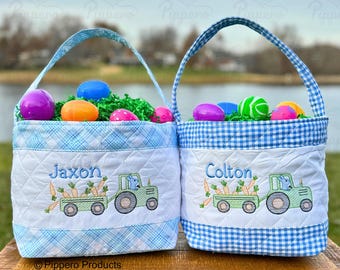 Puede incluir: Dos cestas de Pascua de cuadros azules y blancos con nombres personalizados, Jaxon y Colton, e imágenes bordadas de un conejito tirando de un carro lleno de zanahorias. Las cestas están llenas de huevos de Pascua de plástico de colores y hierba verde.