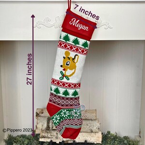May include: A white and red knitted Christmas stocking with a green and white reindeer design. The stocking is 27 inches long and 7 inches wide. The stocking has the name "Megan" written on the cuff.