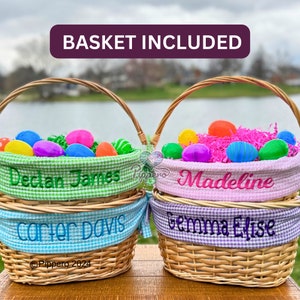 Pode incluir: Duas cestas de P&aacute;scoa de vime repletas de ovos de pl&aacute;stico coloridos e relva de papel rosa. As cestas t&ecirc;m forros de tecido xadrez e nomes bordados: Declan James, Carter Davis, Madeline e Gemma Elise. O texto "Basket Included" est&aacute; no topo.