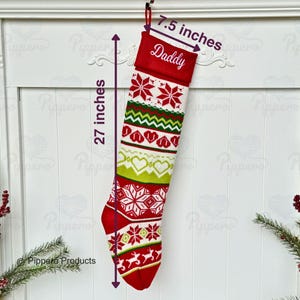 May include: Red and white knitted Christmas stocking with a green, white, and red pattern. The stocking is 27 inches long and 7.5 inches wide. The top of the stocking is red and has the word "Daddy" embroidered on it.