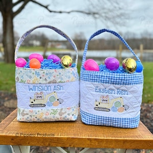 Könnte beinhalten: Zwei personalisierte Osterkörbe aus blau-weißem kariertem Stoff. Die Körbe sind gefüllt mit blauen und rosa Plastik-Ostereiern und blauem zerkleinertem Papier. Die Körbe zeigen gestickte Bilder eines Hasen, der einen gelben Bagger fährt. Der Text "Winston Ash" und "Easten Ren" ist auf die Körbe gestickt.