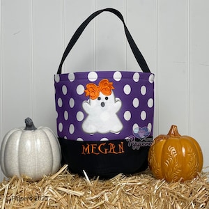 May include: Purple and white polka dot trick or treat bag with a ghost and bow embroidery. The bag has a black handle and the name "Megan" is embroidered on the front.