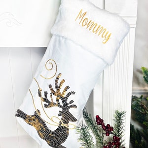 May include: White Christmas stocking with a gold embroidered "Mommy" on the cuff and a black and gold sequined reindeer design.