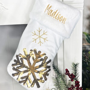 May include: White Christmas stocking with a gold sequin snowflake design and the name "Madison" embroidered on the cuff.