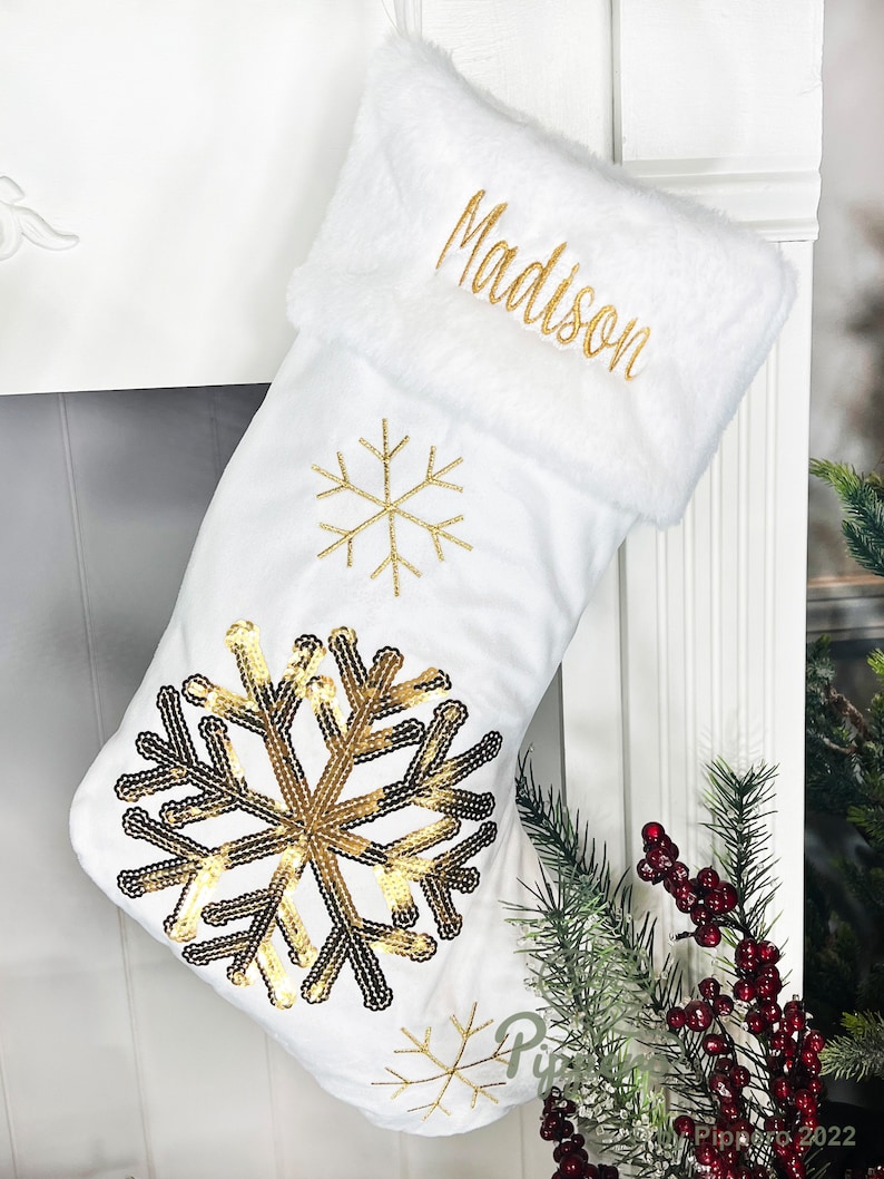May include: White Christmas stocking with a gold sequin snowflake design and the name "Madison" embroidered on the cuff.