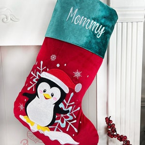 May include: Red and green Christmas stocking with a penguin and snowflakes embroidered on the front. The stocking has a green cuff with the word "Mommy" embroidered on it.