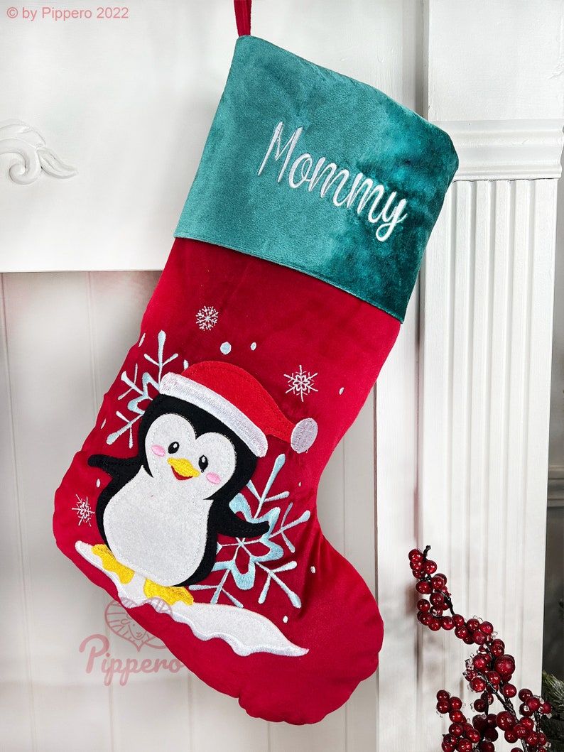 May include: Red and green Christmas stocking with a penguin and snowflakes embroidered on the front. The stocking has a green cuff with the word "Mommy" embroidered on it.
