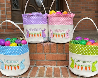 May include: Three personalized Easter baskets with bunny and carrot embroidery. The baskets are blue, pink, and green with white polka dots. The names "Lennox", "Allison", and "Madelyn" are embroidered on the baskets.