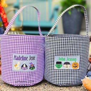 May include: Two gingham fabric Halloween treat bags. One is purple and white, the other is black and white. Each has a rectangular patch with a name and embroidered Halloween characters: a ghost, a vampire, a witch, a Frankenstein, and a pumpkin.