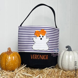 May include: Purple and white striped Halloween trick or treat bag with a ghost and bow applique. The bag has a black bottom with the name Veronica embroidered in orange thread.