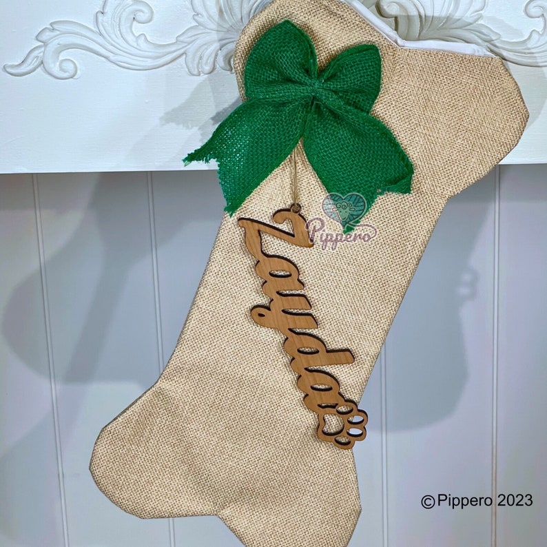 May include: A burlap dog bone stocking with a green burlap bow and a wooden name tag that says "Zayda" with a paw print.