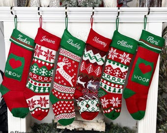 May include: Six red and green Christmas stockings with white snowflake and reindeer patterns hanging on a white fireplace mantel. The stockings are personalized with the names Tucker, Jenson, Daddy, Mommy, Allison, and Rori. The stockings have a red heart with the words "MEOW" and "WOOF" on them.