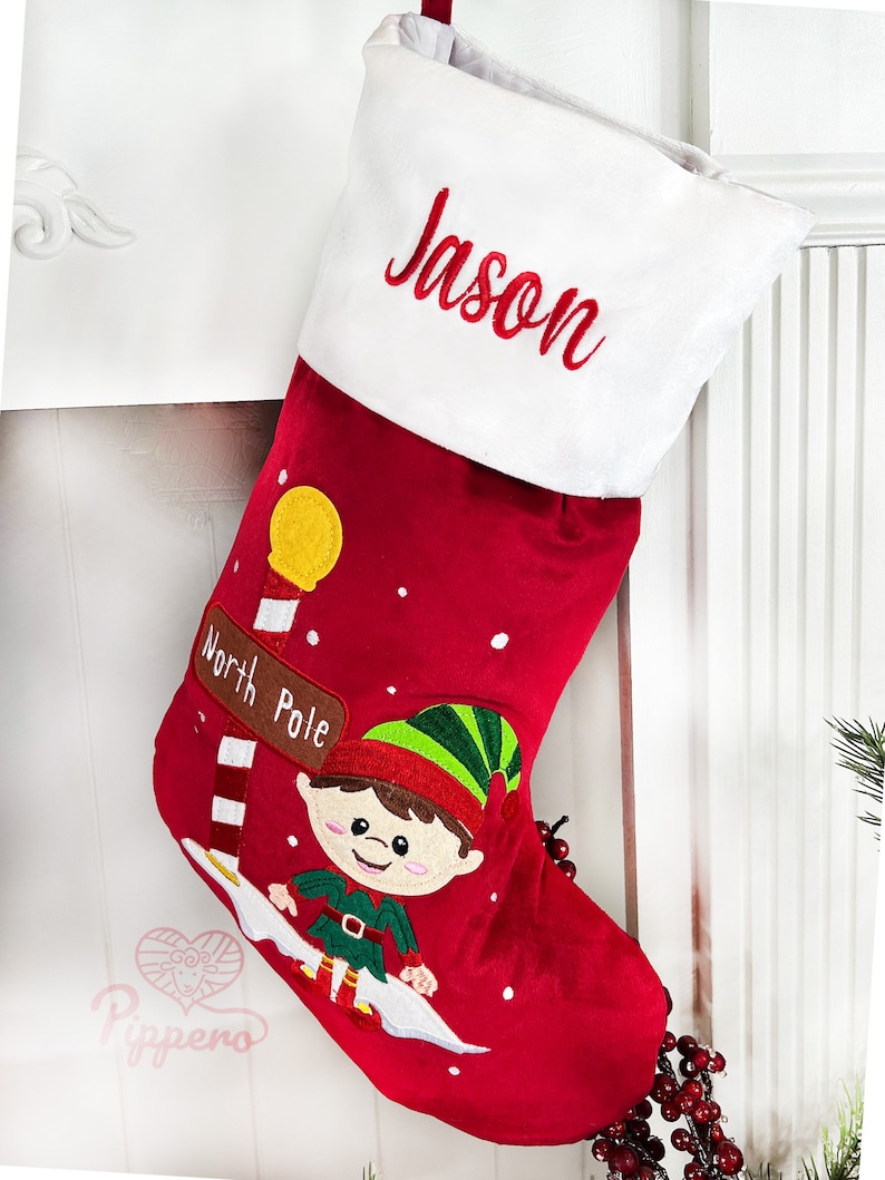 May include: Red Christmas stocking with a white cuff, personalized with the name "Jason". The stocking features an embroidered elf with a green hat and a sign that reads "North Pole".