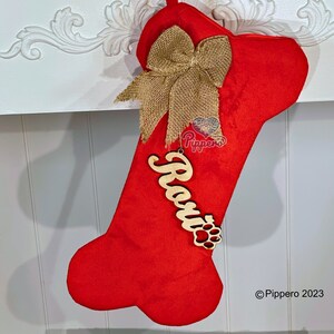 May include: Red dog bone-shaped Christmas stocking with a burlap bow and a wooden name tag that says "Rosie" with a paw print.