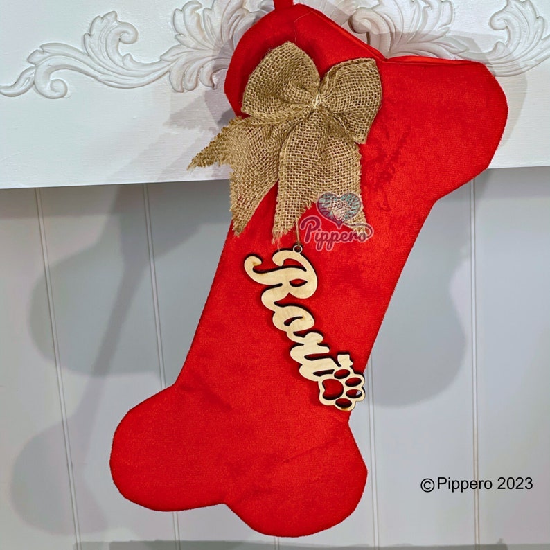 May include: Red dog bone-shaped Christmas stocking with a burlap bow and a wooden name tag that says "Rosie" with a paw print.