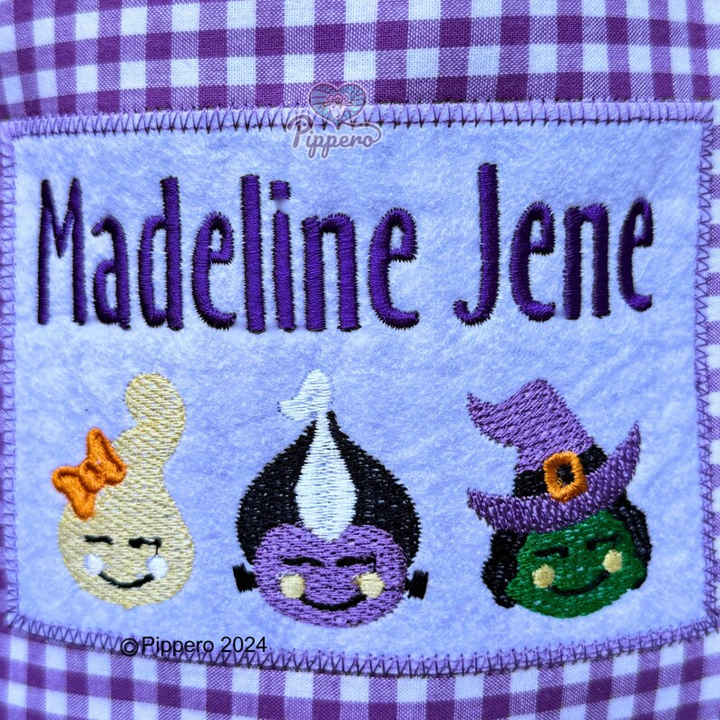 May include: Embroidered patch with the name "Madeline Jene" in purple thread. Below the name are three cartoon Halloween characters: a ghost with an orange bow, a purple monster, and a green witch with a purple hat. The background is light blue.