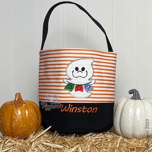 May include: Orange and white striped Halloween trick or treat bag with a ghost holding a "BOO" banner. The bag has a black bottom with the name "Winston" embroidered on it.