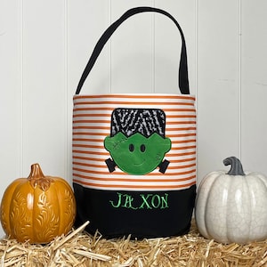 May include: Orange and white striped Halloween trick or treat bag with a green Frankenstein face and the name Jaxon embroidered on the bottom.