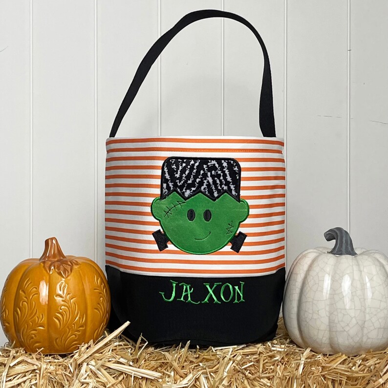 May include: Orange and white striped Halloween trick or treat bag with a green Frankenstein face and the name Jaxon embroidered on the bottom.