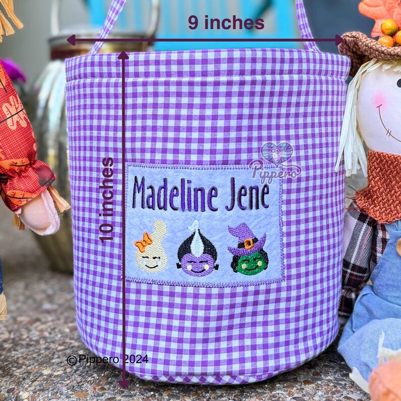 May include: A purple and white gingham fabric tote bag, 9 inches wide and 10 inches tall, with a handle. It features a patch with the name "Madeline Jene" and embroidered Halloween-themed characters: a bunny, a vampire, and a witch.