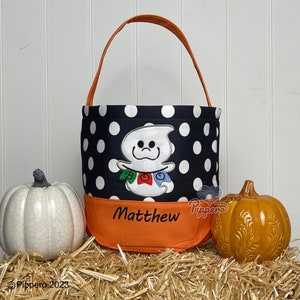 May include: Black and white polka dot Halloween treat bag with an orange top. The bag features an embroidered ghost with a "BOO" banner and the name "Matthew".