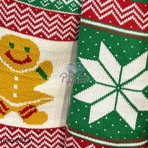 May include: A white knitted fabric with a red and green pattern. The pattern includes a gingerbread man and a snowflake. The gingerbread man is yellow with red and green accents. The snowflake is white with a green background.