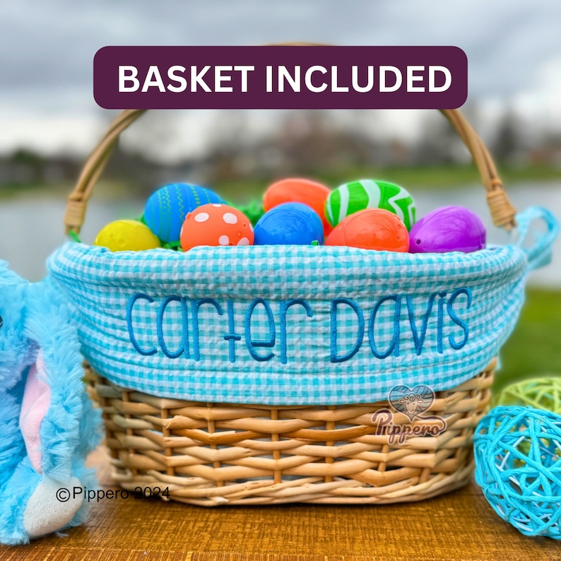 Pode incluir: Uma cesta de P&aacute;scoa de vime com forro xadrez azul e branco. A cesta est&aacute; cheia de ovos de P&aacute;scoa coloridos. O nome "Carter Davis" &eacute; bordado no forro. O texto "BASKET INCLUDED" est&aacute; no topo.