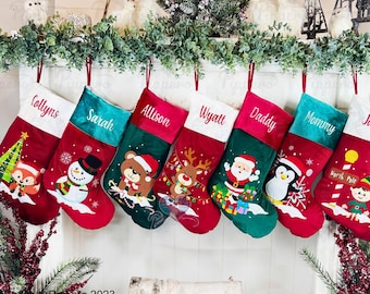 May include: Seven personalized Christmas stockings with various embroidered designs, including a snowman, a bear, a reindeer, Santa Claus, a penguin, a Christmas tree, and a North Pole scene. The stockings are hung on a white fireplace mantel with green garland.