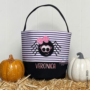 May include: Purple and white striped Halloween trick-or-treat bag with a black spider with pink bow and googly eyes. The bag has a black bottom with the name Veronica in pink letters.