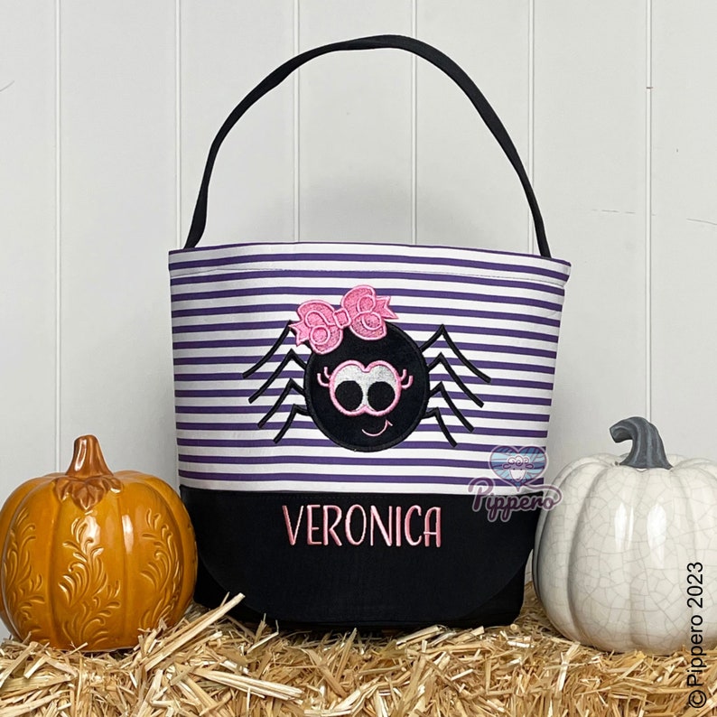 May include: Purple and white striped Halloween trick-or-treat bag with a black spider with pink bow and googly eyes. The bag has a black bottom with the name Veronica in pink letters.